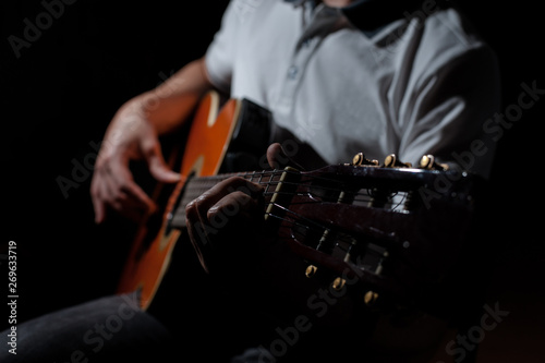Man playing an acoustic guitar on a dark background. Playing guitar