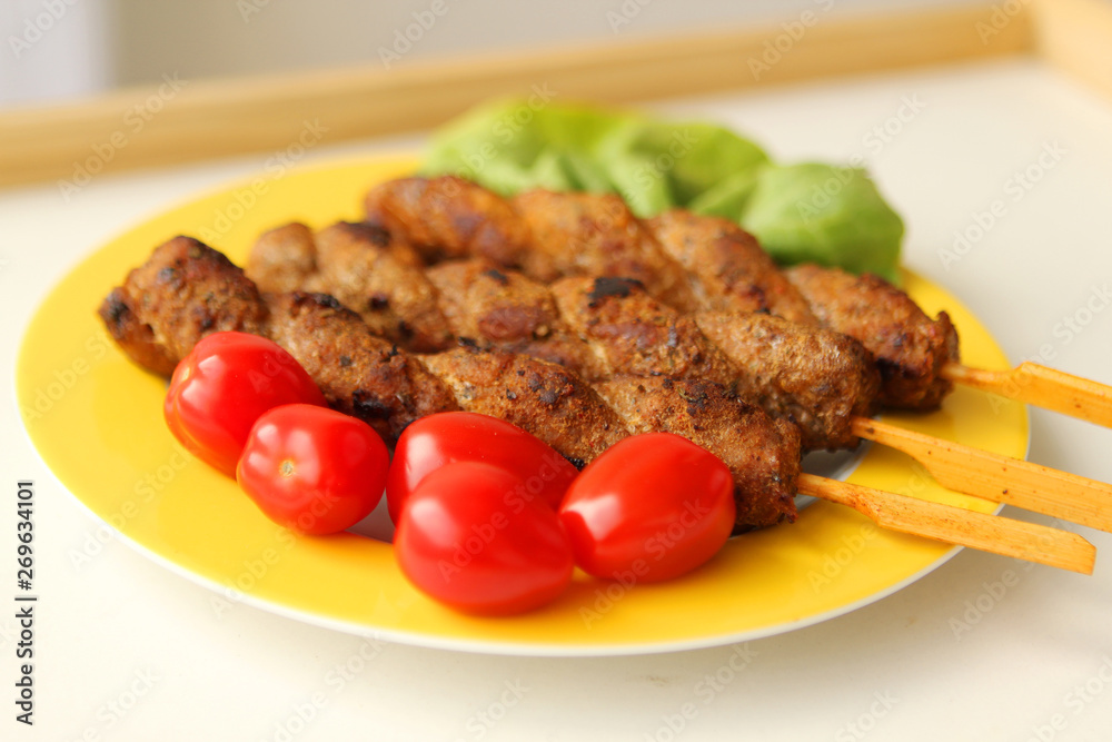grilled meat on skewers fried lies on a yellow plate with fresh vegetables, tomatoes, salad, close-up grilled meat on skewers fried lies on a yellow plate with fresh vegetables, tomatoes, salad, close-up
