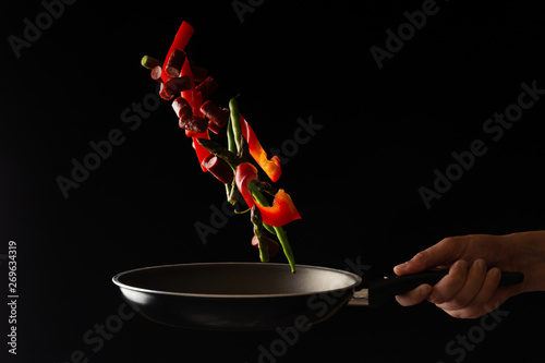 Chef is cooking pepperoni sausages with sweet pepper and spriykovoy beans, on a black background, a recipe book, German sausages