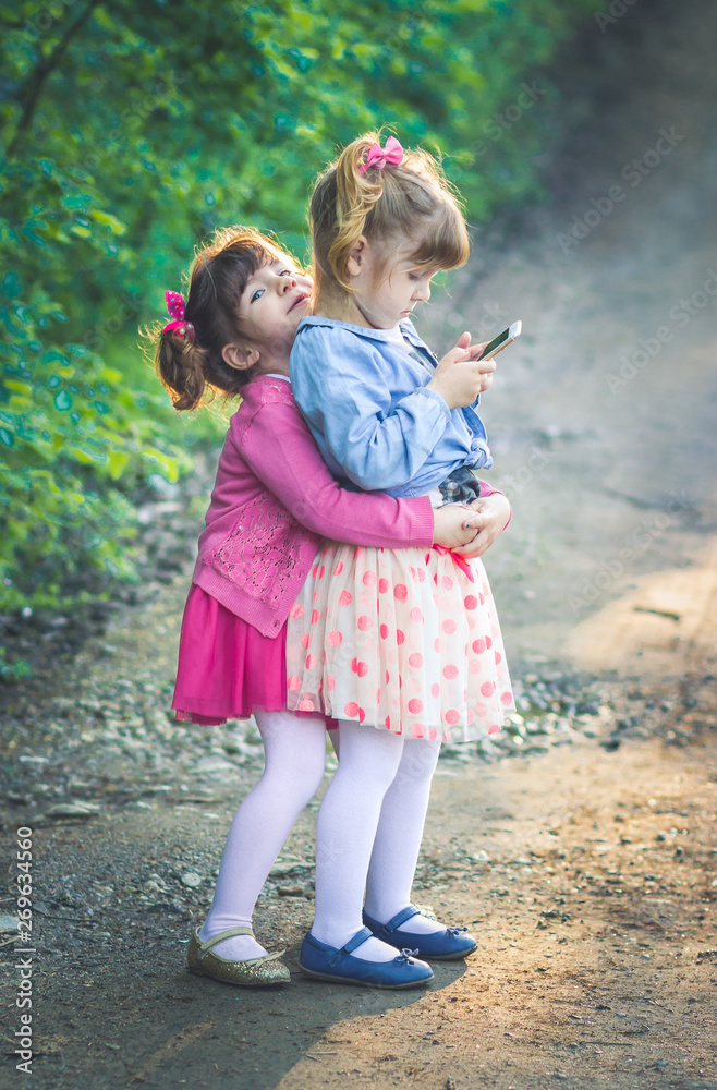 Brunette girl is hugging her sister from behind while shes playing on phone Brunette girl is hugging her sister from behind while shes playing on phone