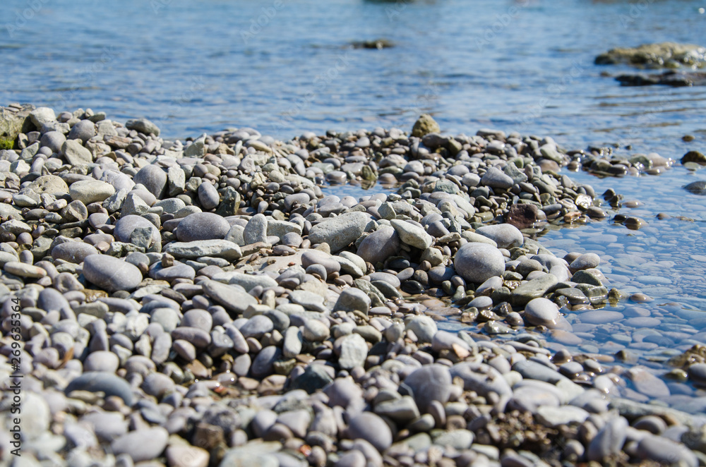 Background of seashore, pebble beach and blue water of sea close up Background of seashore, pebble beach and blue water of sea close up