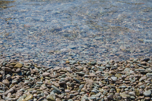 Background of seashore, pebble beach and transparent sea close up