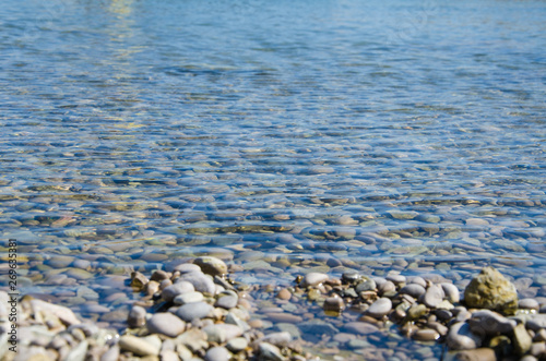 Sea background, ripple surface of transparent water, view of colorful stones bottom underwater