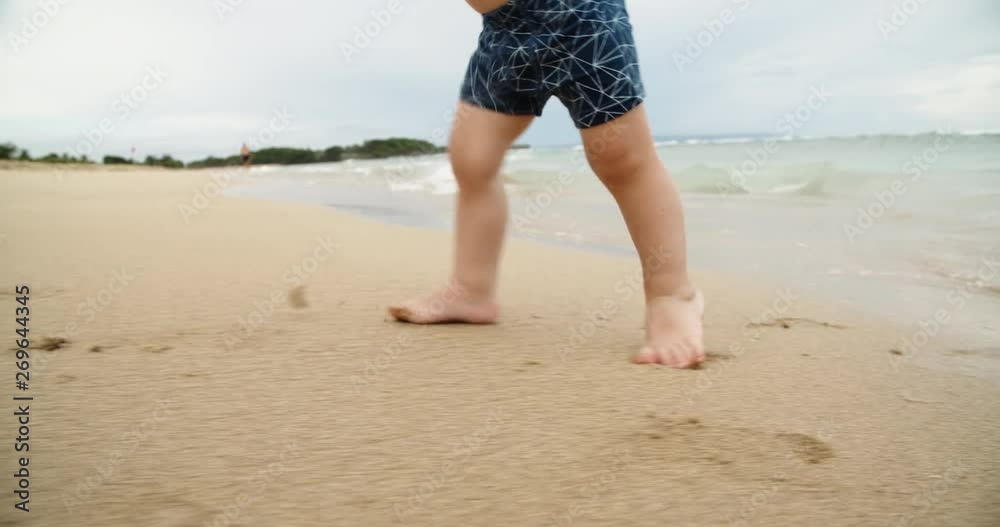 Unrecognizable baby walking down the beach. Cute toddler making careful steps, waves of ocean touching his legs - happy childhood concept slow motion 4k Unrecognizable baby walking down the beach. Cute toddler making careful steps, waves of ocean touching his legs - happy childhood concept slow motion 4k