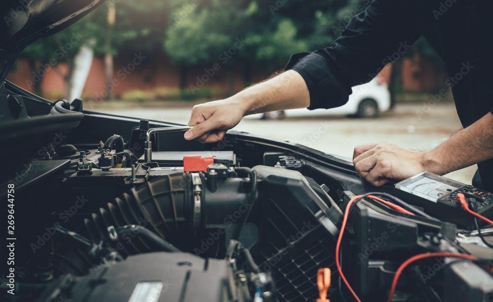 Car mechanic is checking the engine and holding the battery gauge. Car mechanic is checking the engine and holding the battery gauge.