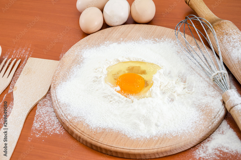 The concept of making dough. Egg chicken in flour, wooden spatula, whisk and rolling pin on a wooden table. The concept of making dough. Egg chicken in flour, wooden spatula, whisk and rolling pin on a wooden table.