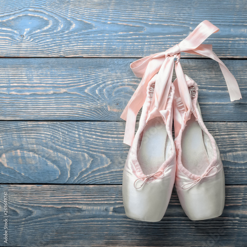 Pointe shoes ballet dance shoes with a bow of ribbons hang on a nail on a wooden background.