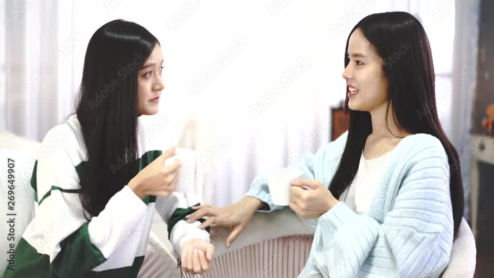 Happy female friends holding coffee mugs while discussing at table in living room relax time.Asian beauty woman smile and sititing sofa . Happy female friends holding coffee mugs while discussing at table in living room relax time.Asian beauty woman smile and sititing sofa .