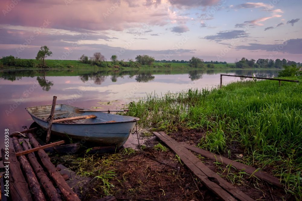 Obraz premium Picture of a row boat on Russian river Nerl on sunset. Blue sky and amazing clouds