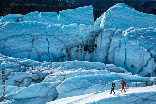 Man and woman walking narrow ridge on the Matanuska Glacier in Remote Alaska. Large crevasses and fins break up the ice all around them.