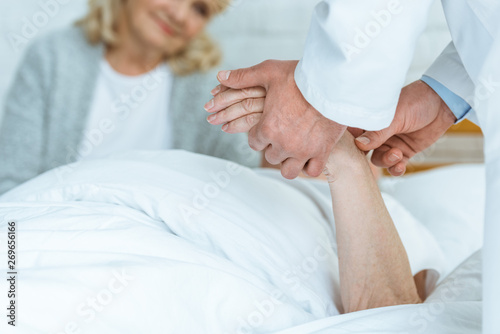 partial view of doctor standing near patient and checking pulse