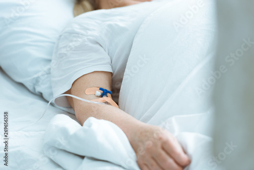 partial view of sick woman lying on bed during intravenous therapy in clinic