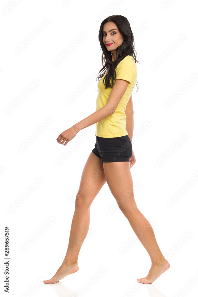 Beautiful Young Woman Is Walking Barefoot, Looking At Camera and Smiling. Side View. Beautiful Young Woman Is Walking Barefoot, Looking At Camera and Smiling. Side View.