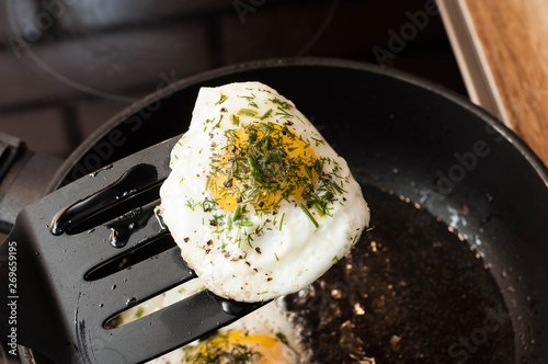 Fried egg with herbs and pepper on a spatula over the pan ready to eat as a perfect breakfast