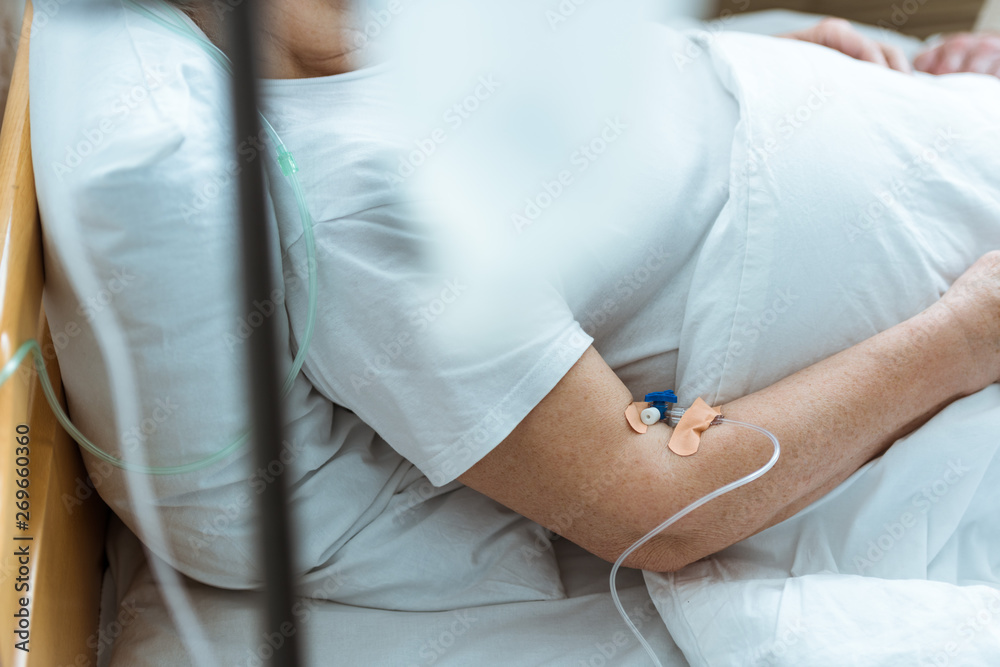 partial view of sick woman lying on bed during intravenous therapy in clinic partial view of sick woman lying on bed during intravenous therapy in clinic