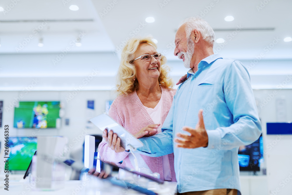 Fototapeta premium Happy smiling senior choosing new tablet while standing in tech store.