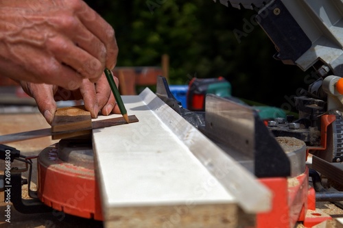 Preparation for cutting with a electric chop saw. male Hand of carpenter is measuring angle of a board. marking wood board next to professional electric chop saw on work table on construction site.
