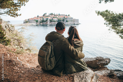 A young couple of tourists admires the beautiful view of the sea and the island of Sveti Stefan in Montenegro.