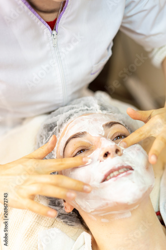 Happy young woman receives a facial treatment in spa center