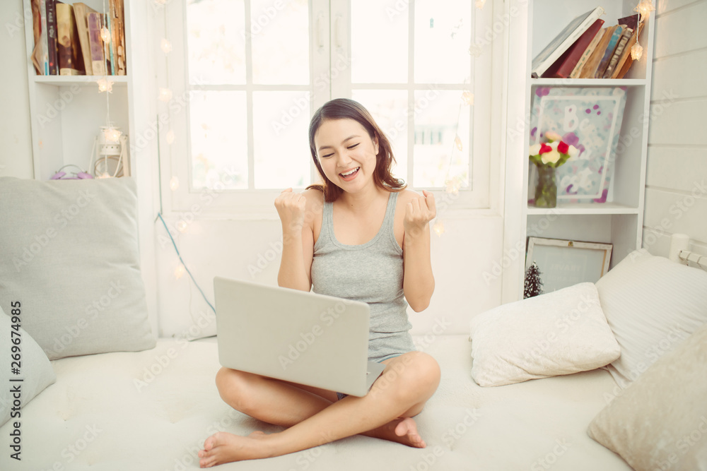 Happy asian woman using laptop while sitting on bed in the morning Happy asian woman using laptop while sitting on bed in the morning