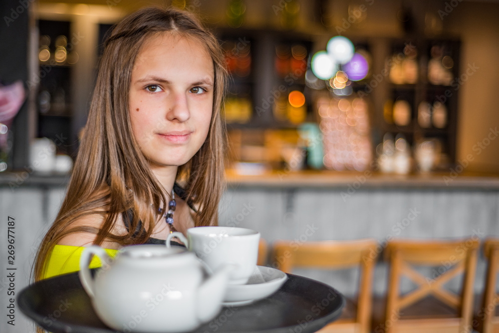 Portrait young waitress standing in cafe. girl the waiter holds in bunches a tray with utensils. Restaurant service