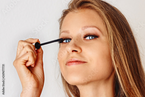 Beautiful woman holds brush of mascara and puts on cosmetics on her face. Make-up  cosmetics  beauty  eye lash extension