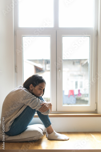 Sad depressed young woman having social problems sitting on windowsill