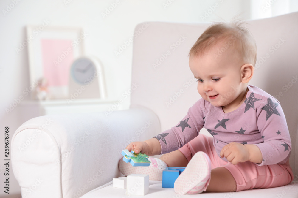 Cute baby girl playing with building blocks in armchair at home. Space for text Cute baby girl playing with building blocks in armchair at home. Space for text