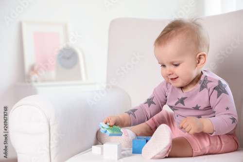 Cute baby girl playing with building blocks in armchair at home. Space for text