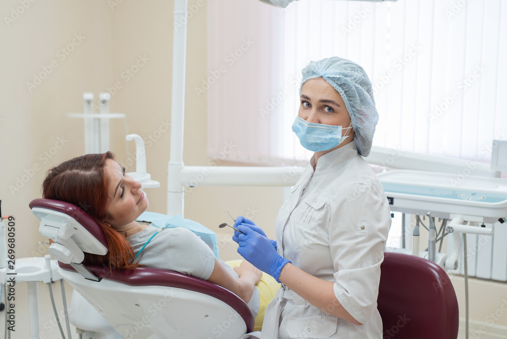 Young beautiful female dentist helps patient with toothache. Red-haired woman sits in a chair at the doctor on examination. Dental services. Young beautiful female dentist helps patient with toothache. Red-haired woman sits in a chair at the doctor on examination. Dental services.