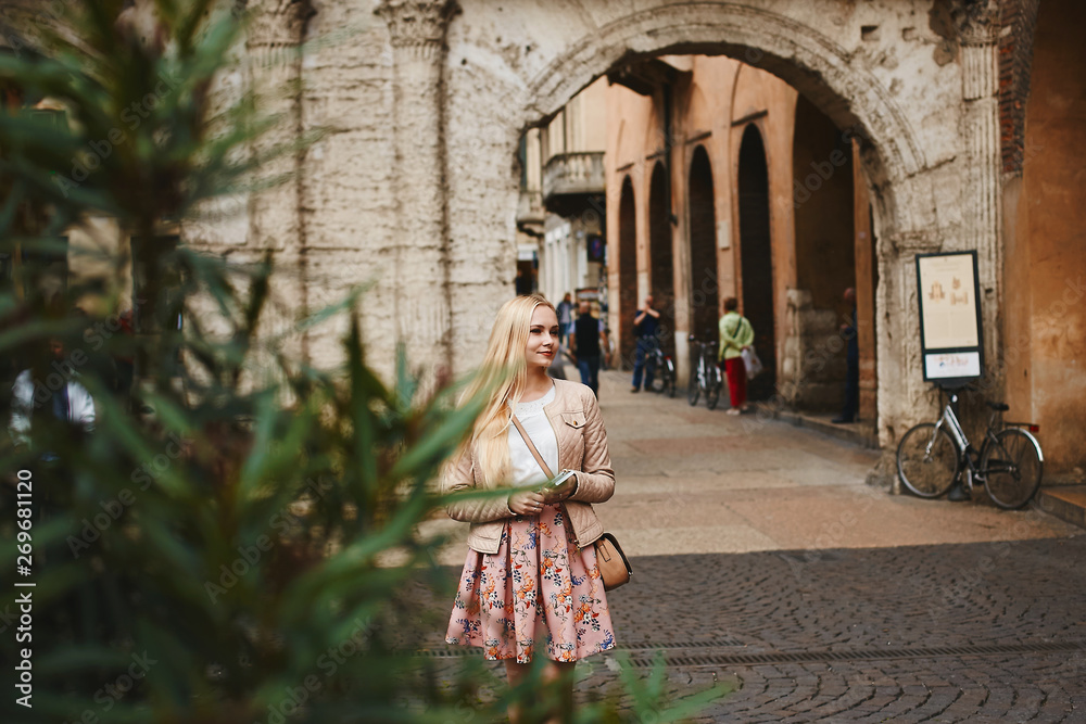 Beautiful and young blonde model woman in a pink skirt, in white blouse and in leather jacket waiting for someone at the ancient street at Verona, Italy Beautiful and young blonde model woman in a pink skirt, in white blouse and in leather jacket waiting for someone at the ancient street at Verona, Italy