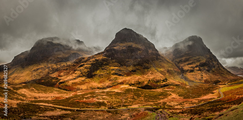 A moody panoramic of the Three Sisters mountains in Glencoe, covered in rusty moorlands. Scotland