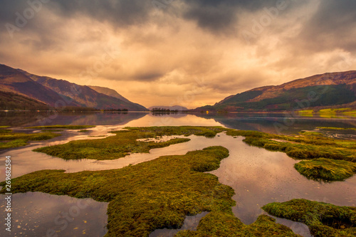 Loch Leven at sunset with grassy mounds and streams of water in the foreground and mountains in the distance. Scotland. © Jennifer