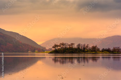 Loch leven at sunset, with mountains in the background and an island of trees reflected in the water. Glencoe, Scotland.