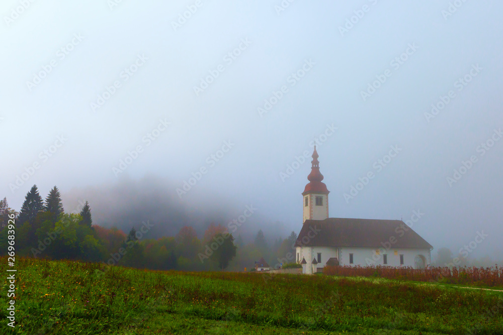Church in the field near the forest in the morning mist. Orange and brown colors of fading nature.