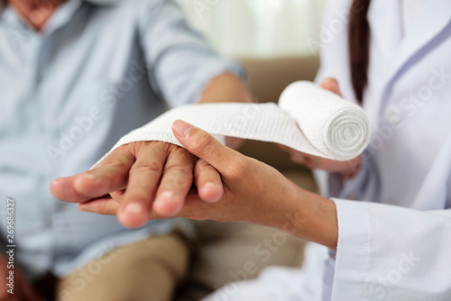 Schilderij op canvas Close-up of female doctor putting a bandage on injured hand of senior man at hos