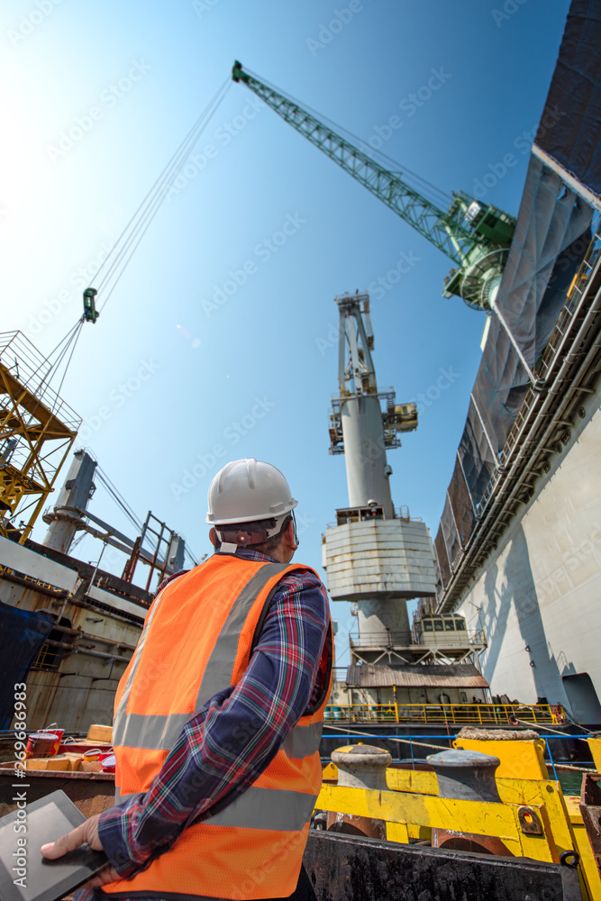 stevedore or foreman, engineering, loading master talks to crane driver by walkie talkie for safety lifting the goods shipment, lifting by gantry crane, working at risk on the high level insurance