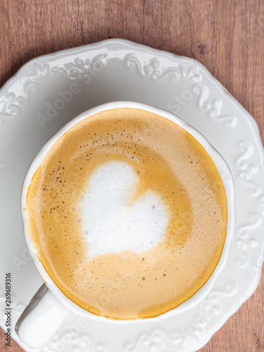 Close up white coffee cup with heart shape latte art on wood table at cafe.
