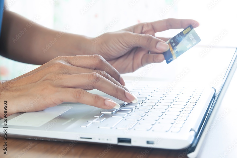 Fototapeta premium Woman hand holding plastic credit card and using laptop computer. Online shopping, paying, buying, e-payment and technology concept.