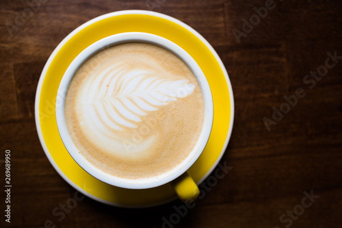 Yellow cup of aromatic coffee on a wooden table.