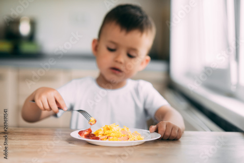 child day in the kitchen eating an omelet with sausage and ketchup