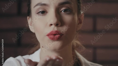 Sexy woman with red lips sending kiss from hand to camera on brick background