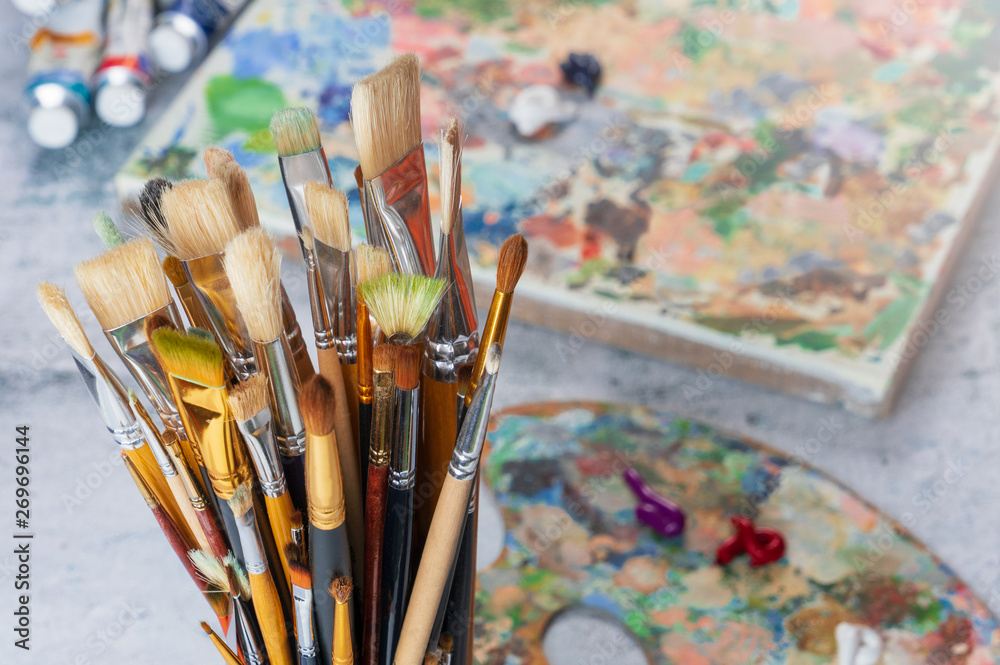Obraz premium Paint brushes in a glass close-up on the background of a palette, paints and canvas.