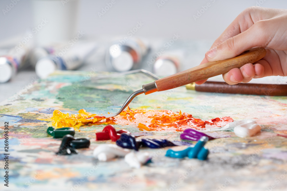 A young girl holds in his hand a palette-knife for drawing and mixes oiled paints. The process of mixing colors on the palette. A young girl holds in his hand a palette-knife for drawing and mixes oiled paints. The process of mixing colors on the palette.