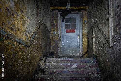 Creepy dark yellow hallway with peeling paint leading to stairs and scary door in an abandoned school