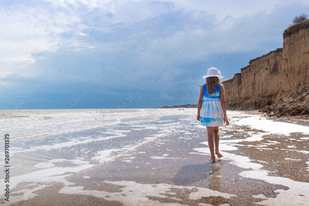 Beautiful girl in white hat and colorful dress on the seashore over blue sky background