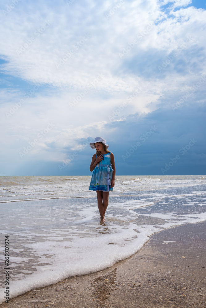 Beautiful seascape. Girl in dress and white hat on the beach over blue sky background