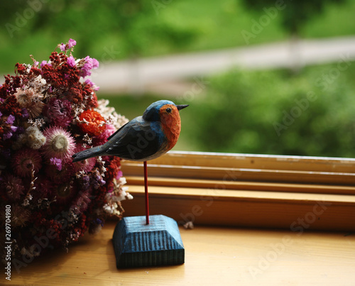 souvenire wooden figure of little bird robin   and a bouquet on the windowsill against nature spring background photo