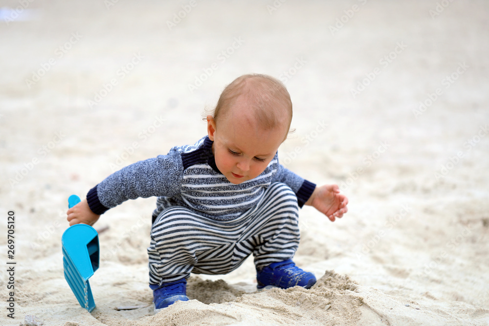 Baby Boy Playing With Sand And Blue Plastic Shovel On The Beach Baby Boy Playing With Sand And Blue Plastic Shovel On The Beach