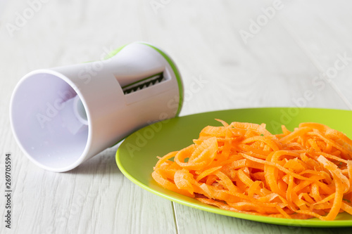 Carrot grated on a green plate with a grating cutting kitchen utensil with a grey wood background photo